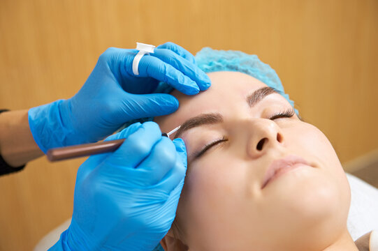 Permanent make-up master makes eyebrow correction procedure. Permanent makeup. Close-up.