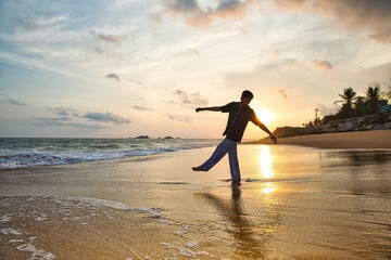 An adult man standing on the shore of the Sea, with the sun setting behind him. Dammam, Saudi Arabia. 