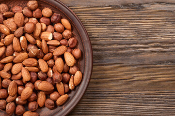 Different nuts in plate on a wooden background. Almond and hazelnut.