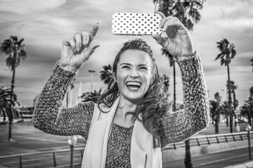 in Barcelona for a perfect winter. happy young woman on embankment in Barcelona, Spain  taking photo with phone