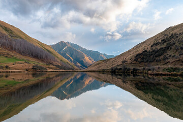 Photograph of Lake Kirkpatrick with mountains reflecting in the water on a cloudy day outside Queenstown on the South Island of New Zealand