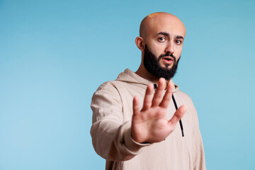 Young serious arab man showing prohibition gesture with palm portrait. Person making stop and rejection signal with hand while looking at camera with confident facial expression