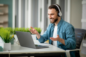 Video Call. Cheerful Young Businessman In Headphones Making Teleconference In Office