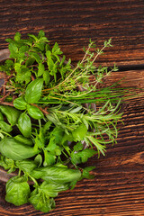 Various aromatic culinary herbs. Fresh thyme, marjoram, basil, mint, chives and parsley herbs on plate on old brown wooden background, top view. Rustic, vintage, natural, country style images.
