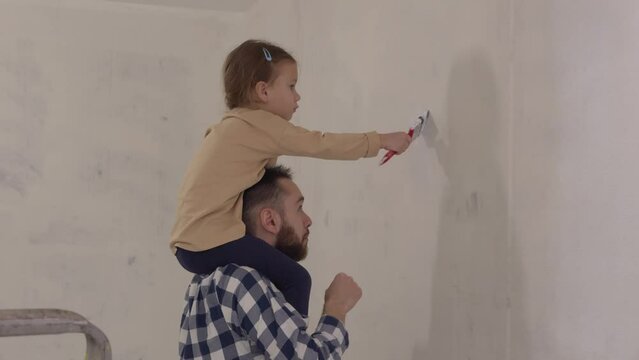 Dad and doughter making repair works painting wall together. Happy family make renovation DIY renew home concept. Child girl helping parents to redecorating in new apartment. 