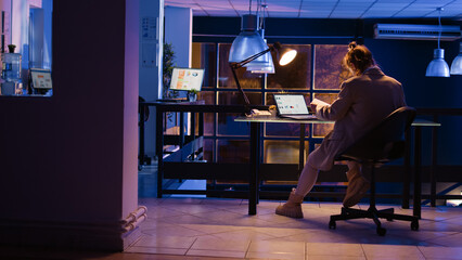 Obraz premium Advisor agent checking corporate report late at night, working overtime to develop new marketing strategy. Office manager planning financial graphs project on monitor. Handheld shot.