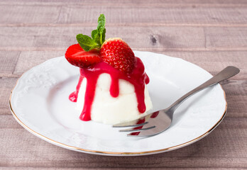 panna cotta dessert with strawberry sirup and mint leaf on light wooden background