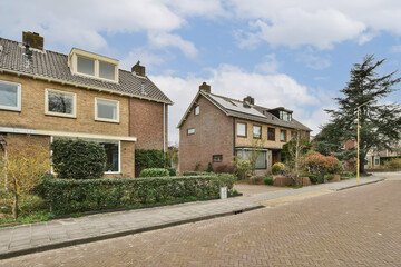 an empty street in the netherlands with houses and trees on either side, there is a cloudy blue sky above
