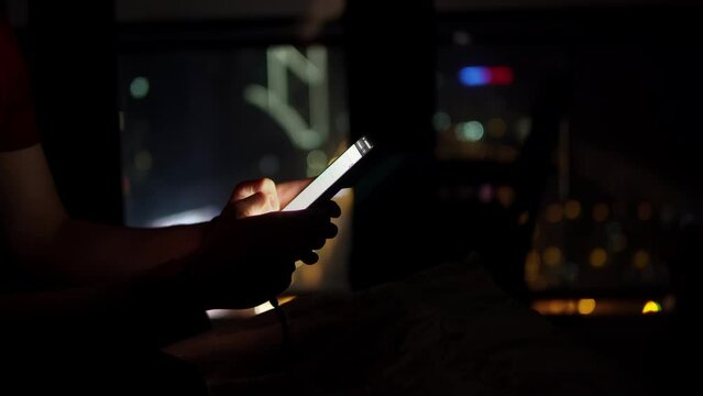 Closeup view of male hands holding smartphone and surfing the internet swiping and tapping on touch screen. Man is sitting in the darkness at home and reading news in mobile phone. Modern gadget theme