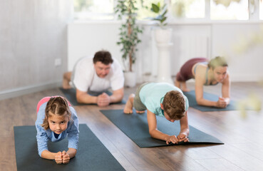 Parents together with children in yoga pose upward-facing dog at gym