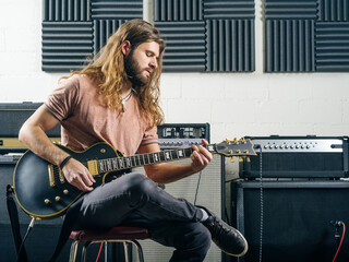 Photo of an attractive man playing electric guitar in a recording studio.