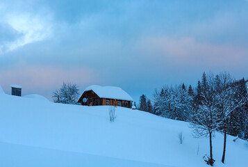 Wooden house on winter hill top in evening Ukrainian Carpathian Mountains (cloudy weather).
