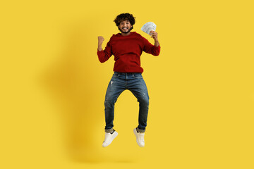 Fototapeta na wymiar Happy rich young indian guy holding money cash, jumping up