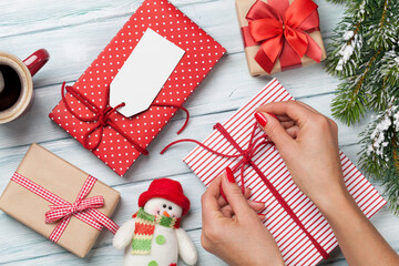 Female hands wrapping christmas gift box above wooden table. Top view with copy space