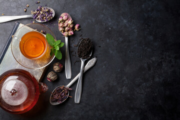 Tea cup, teapot and assortment of dry tea in spoons on stone table. Top view with copy space