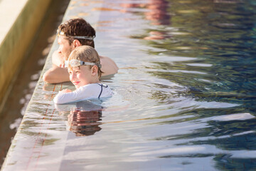 family of two, father and son enjoying together at infinity pool at resort