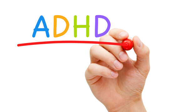 Hand writing ADHD Attention Deficit Hyperactivity Disorder with marker on transparent glass board.