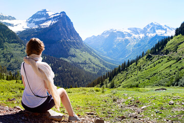 back view of young woman enjoying gorgeous mountain and valley view in glacier national park,...