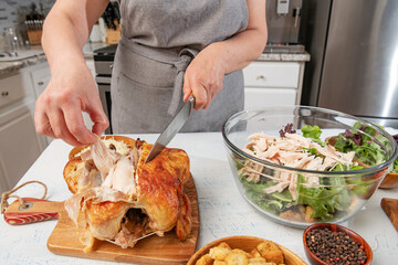 woman prepares a caesar salad in the kitchen. Pieces of fried chicken are added to the salad bowl. Knife and hands close-up.