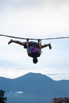 Vertical shot of an extreme slackliner hanging upside down with his hands to the tightrope and split legs  