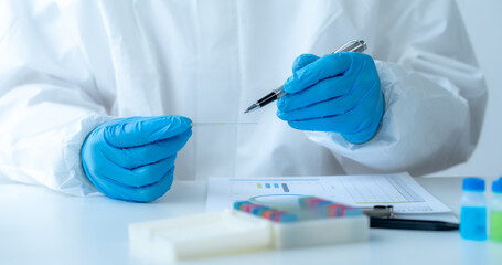 Doctor hand taking a blood sample tube from a rack with machines of analysis in the lab background,...