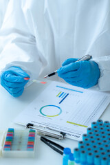 Doctor hand taking a blood sample tube from a rack with machines of analysis in the lab background,...