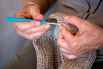 detail of sixty year old woman's hands making crochet bag, low crochet stitch with plastic handle,...