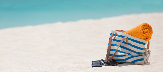panorama of beach bag, towel and flip-flops at white sand perfect caribbean beach with turquoise water in the background at anguilla island, vacation concept, copyspace on the left