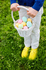 little boy holding white basket with easter eggs after egg hunt standing at grass in the park