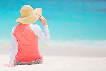 back view of woman in rashguard and sunhat enjoying picture perfect caribbean beach with turquoise...