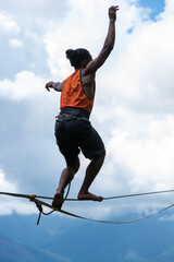 Vertical shot Slackliner on a rope balancing standing with a man's bum and orange shirt. With...