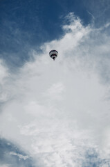 Flying hot air balloon against a blue sky with clouds.