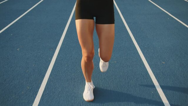 Slender sporty female legs running on athletics track in the stadium outdoors. Sweaty sexy legs in skintight shorts, white socks, snickers. Track sections. High quality 4k footage