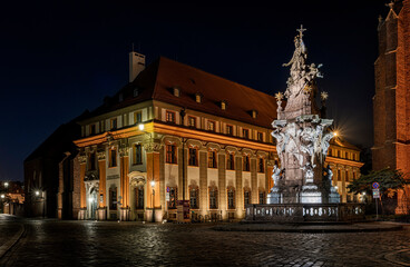 Obraz premium Illuminated, brick buildings and tall monument in Ostrow Tumski in Wroclaw at night.
