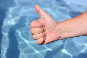 A person hand with a thumbs up, a sign of approval, on the background of the pool