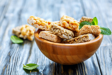 Honey bars with peanuts, sesame seeds and sunflower seeds in a wooden bowl on an old table, selective focus.
