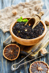 Wooden bowl with black tea, sugar cane and sugar tongs on an old kitchen table, selective focus.