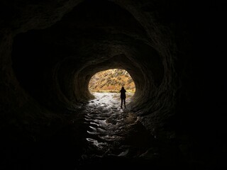 Silhouette of a person standing in dark black natural water tunnel at Broken River Cave Stream...