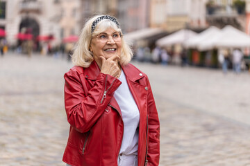 Fototapeta premium Thoughtful pensive puzzled senior woman with pensive expression, pondering a solution, doubting question, thinking inspiration dreaming outdoors. Mature grandmother in city street. Town lifestyles