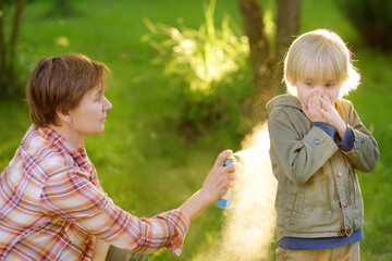 Woman spraying insect or mosquito repellents on little boy before a walk in the forest. Protect...