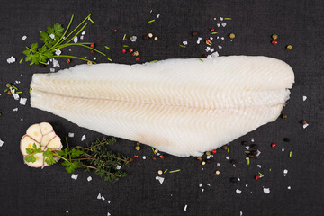 Fresh halibut fillet with fresh herbs and garlic on dark black stone background top view. Luxurious...