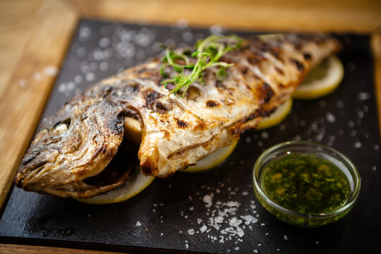 Grilled dorada fish with lemon and spinach served on a stone board