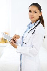 Young brunette female doctor standing and smiling at hospital.  Physician ready to examine patient