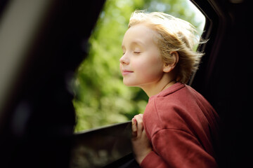 Cute preteen boy inhales the air of freedom from car window during family road trip and enjoy of...