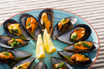 Baked mussels with sauce of oil, garlic and parsley served with lemon slices on color plate..