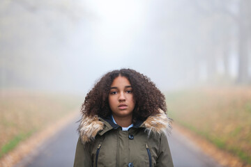 Outdoor portrait of beautiful mixed race African American girl teenager female child outside in  a park on foggy day