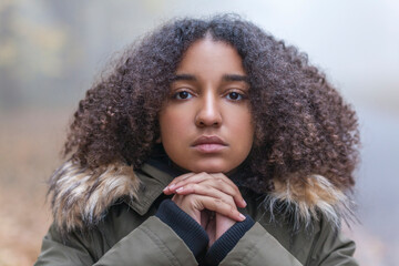 Outdoor portrait of beautiful mixed race African American girl teenager female child resting on her hands outside in  a park on foggy day © Designpics