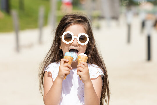 Beautiful little girl in sunglasses and white summer shirt eating an ice cream. High quality photo