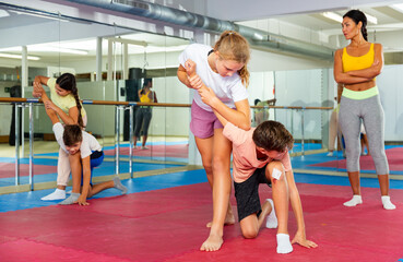 Fototapeta na wymiar Focused kids in pair exercising self-defense movements during group class with female coach