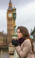 Girl or young woman drinking coffee in a disposable cup on Westminster Bridge with Big Ben in the...